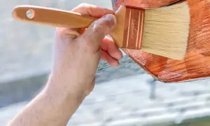 Mano aplicando barniz a madera de pino para exterior. Protegiendo la madera para que dure más.