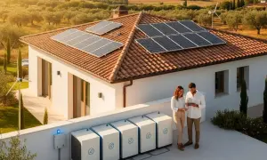 Pareja revisa tablet junto a baterías de autoconsumo en Navarra. Paneles solares y aerogenerador en tejado de casa rural.