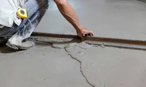 Obrero usa regla para nivelar suelo con tableros de cemento fresco.
