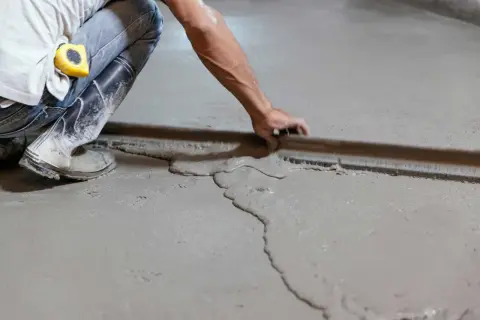 Obrero usa regla para nivelar suelo con tableros de cemento fresco.