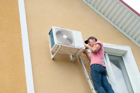 Técnico instala unidad exterior de aire acondicionado. Se aprecian las dimensiones de la unidad y el trabajo en la fachada.
