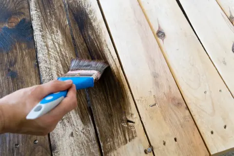 Aplicando tinte oscuro a madera sin tratar con una brocha. El proceso de pintar madera sin tratar transforma su aspecto.