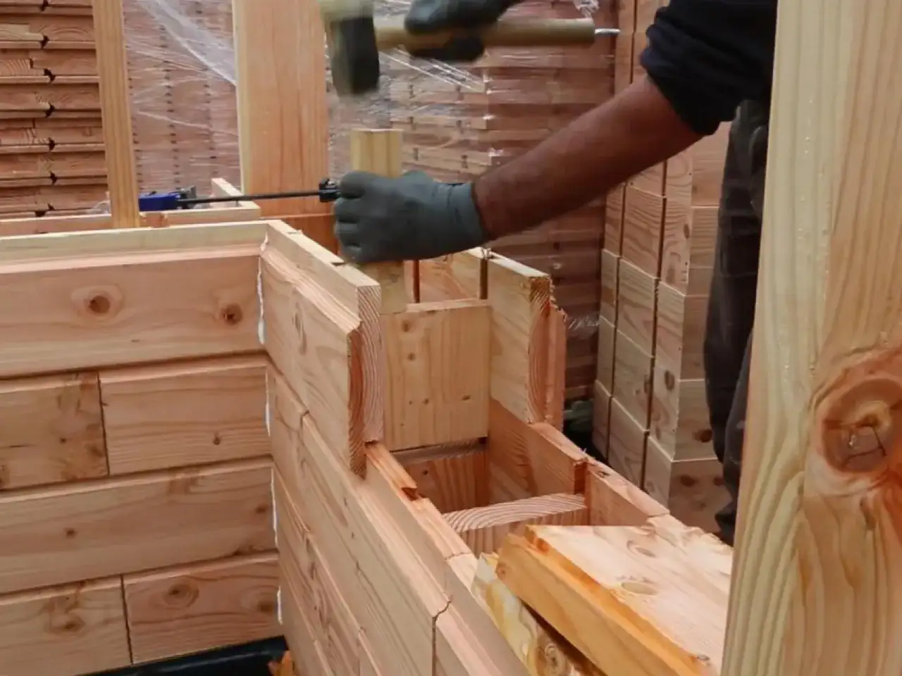 Construcción de una cabaña con madera aislante térmico. Un trabajador martilla una pieza de madera para encajarla.