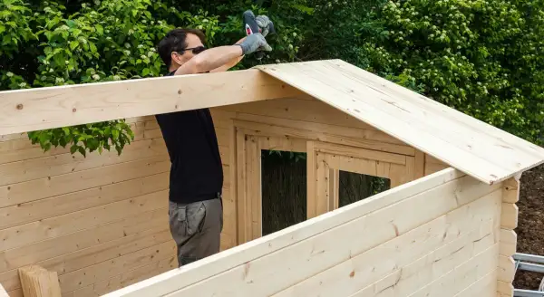 Hombre construyendo una caseta de madera. ¿Cuál es la mejor madera? Esta parece ser de pino, ligera y fácil de trabajar.