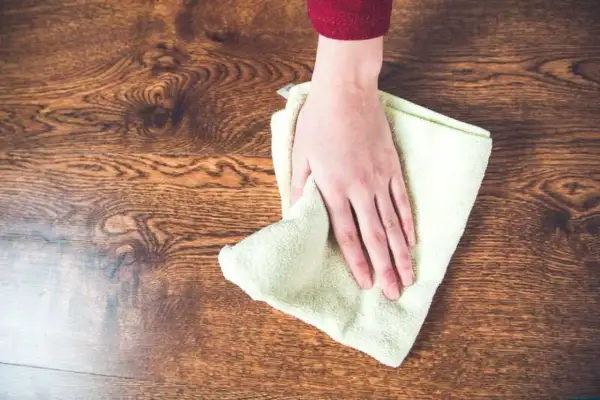Mano limpiando un suelo de madera con un paño, aprendiendo como quitar manchas de la madera sin dañarla.